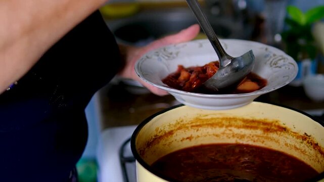 female hands pouring plate of borscht from yellow pot enjoys traditional homemade borscht with sour cream, garlic and lard. Cozy kitchen atmosphere, hearty lunch or dinner and authentic comfort food.