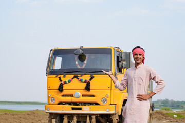 Smiling Indian truck driver posing proudly beside a yellow dumper truck on a rural roadside © Niks Ads