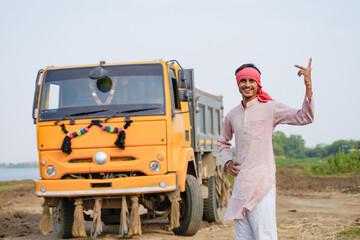 Smiling Indian truck driver posing proudly beside a yellow dumper truck on a rural roadside © Niks Ads