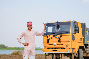 Smiling Indian truck driver posing proudly beside a yellow dumper truck on a rural roadside © Niks Ads