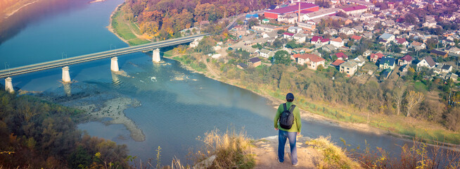 A man stands on a hill and looks at a fantastic view of the winding Dniester River at dawn in the fall. Dniester Canyon National Park, Zalishchyky town, Ternopil region, Ukraine © vvvita