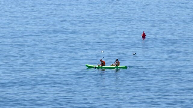 Two People Paddling a Green Kayak on the Calm Blue Sea