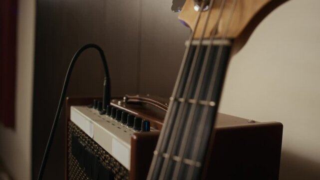 Rack focus shot of bass guitar next to vintage amplifier in recording studio during band rehearsal. Footage is suitable for music education, instrument promotion, or audio production marketing