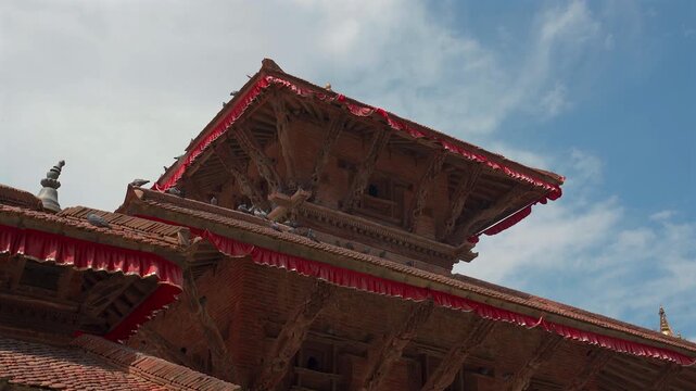 Low angle view of the intricate hand-carved wooden struts and tiered roofs of an ancient pagoda temple decorated with red fringe at Kathmandu Durbar Square, Nepal.