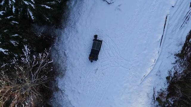 Solar-powered vehicle on snowy forest road as drone descends and rotates above winter landscape in Parc naturel r&eacute;gional du Haut-Jura, France; evergreen trees and icy track.