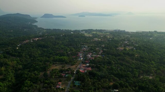 Cinematic pullback aerial reveal of moody sunrays shining through clouds above tropical countryside and Taal Lake in Gonzales Batangas.