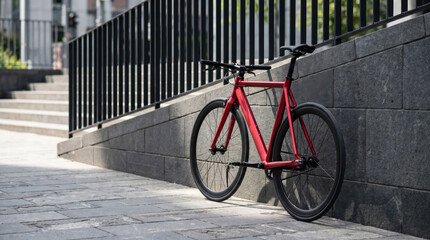 Obraz premium Minimalist urban scene with stylish red bicycle leaning against concrete wall beside pedestrian pathway, showcasing eco friendly mobility, sustainable city commuting and modern urban cycling lifestyle