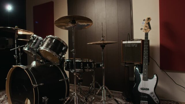 Drum kit, cymbals, and electric bass guitar standing ready in empty music recording studio. Footage is suitable for music education, band rehearsal promo, or audio production advertising
