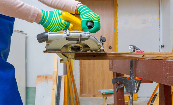 Woman carpenter using circular saw to cut wooden board. Professional woodworker performing home renovation. Diy project and construction site with power tool in workshop. Industrial skill