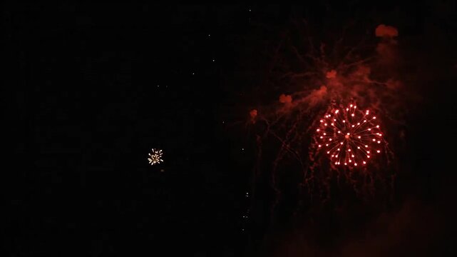 Bright orange and red fireworks explode in the dark night sky during a celebration