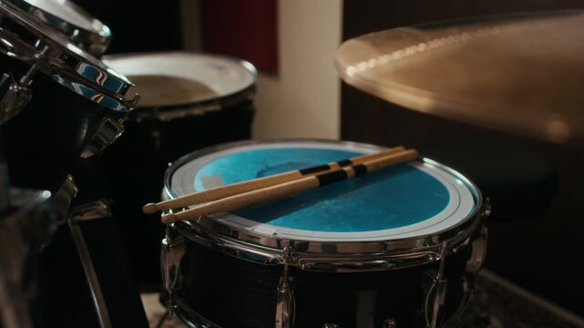 Drumsticks resting on blue snare drum in recording studio during band rehearsal. Footage is ideal for music school advertisements, instrument retail marketing, and creative arts education promos