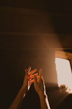 Hand reaching up into warm sunbeam in dark room
