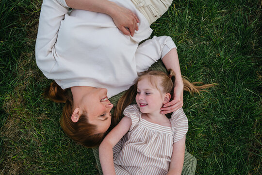 Mother and daughter lying on grass smiling at each other