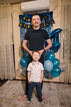 Happy father hugging and congratulating his little son in a blue birthday photo zone, dad and child celebrating a 4th birthday party.