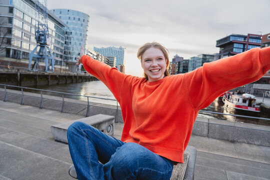 Happy youth sitting with arms outstretched at HafenCity harbor