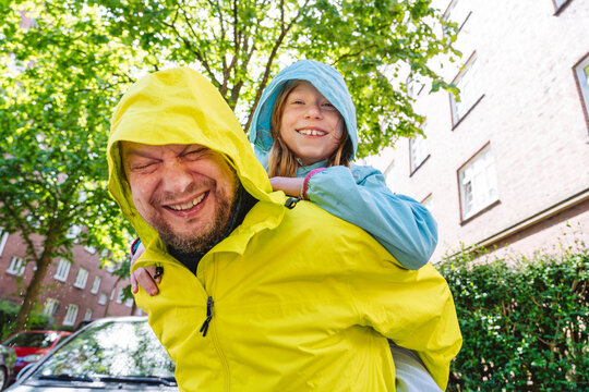 Smiling father giving daughter a piggyback ride in raincoats