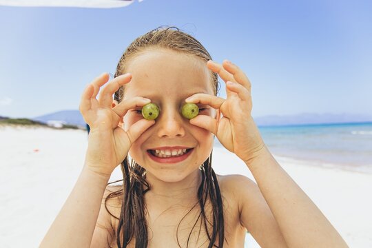 Child playing with green grapes on the beach during summer vacation