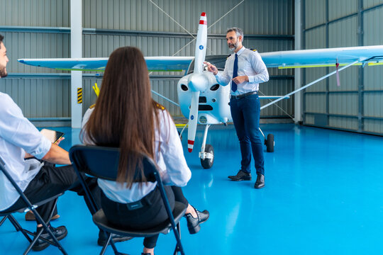 Pilot instructor teaching aviation students in airplane hangar