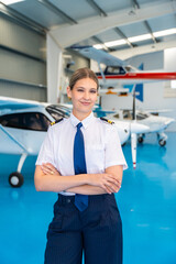 Fototapeta premium Confident female pilot standing in aircraft hangar