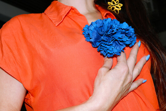 Hand touching blue carnation on orange shirt at Feria de Abril