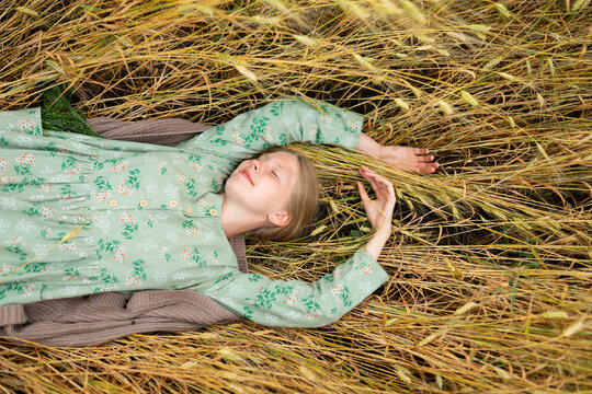 Woman relaxing in a summer wheat field wearing a vintage floral dress