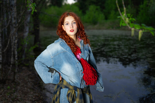 Red-haired model in denim jacket standing by a forest swamp