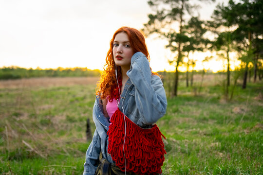 Red-haired model in denim jacket listening to music outdoors