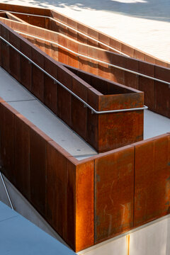 Rust wall terraces step through modern architecture in an urban outdoor detail, where railing, concrete and sunlight reveal warm geometric texture