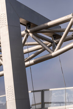 Steel beams cross modern architecture beside a column, where structure, cable and sky turn an urban exterior into an abstract construction detail