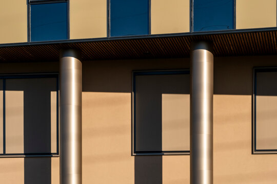 Modern facade with columns and windows catches warm sunlight, turning urban architecture into an abstract detail of shadow, rhythm and surface
