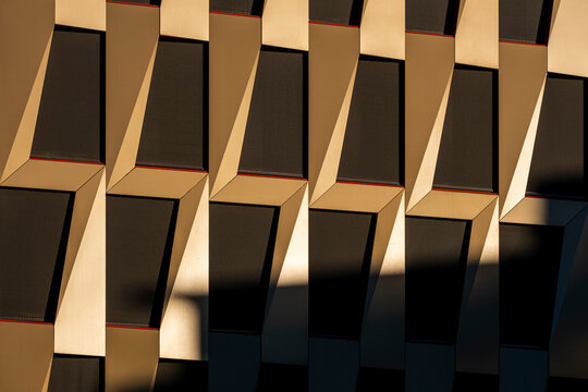Angled windows and deep shadow create a geometric facade on modern architecture, where sunlight sharpens urban pattern across the building surface