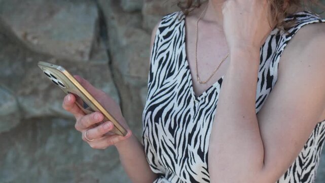 Smartphone woman browsing young lady in zebra print dress using mobile phone outdoors while standing near a stone wall