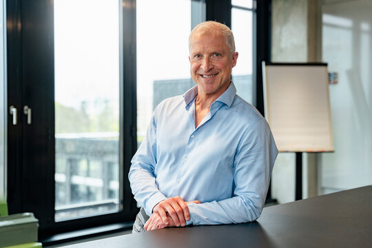Smiling managing director leaning on desk in modern office