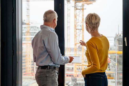 Architect and manager looking out office window at construction site