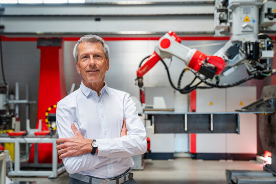 Smiling manager standing in automated factory with industrial robot