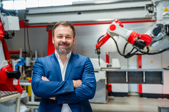 Smiling manager in suit at factory with industrial robot