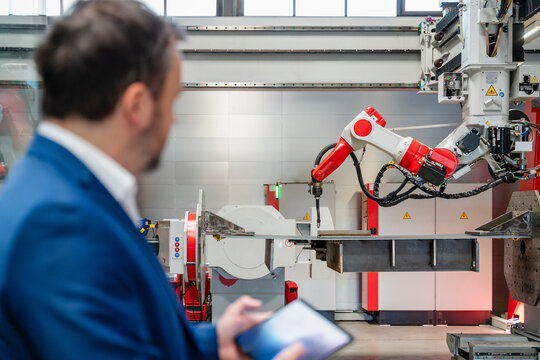 Manager with tablet monitoring industrial robot in factory