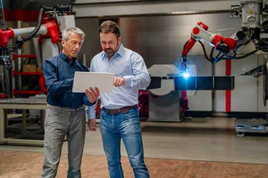 Engineers using tablet near industrial welding robot in factory