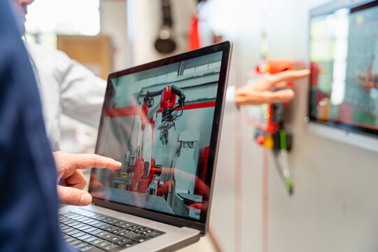 Employee pointing at laptop screen showing industrial robot