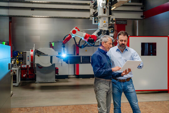 Staff using tablet near welding robot in factory