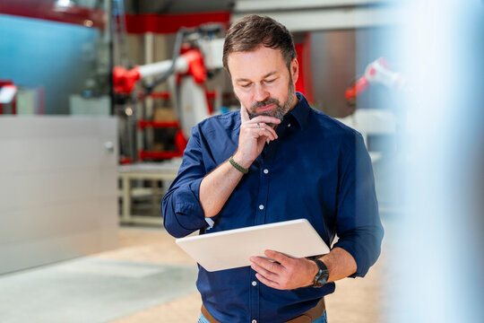 Thoughtful engineer holding tablet in automated factory