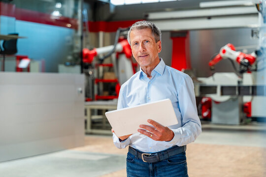 Smiling engineer holding tablet in automated factory