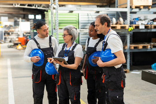 Industrial team discussing project on tablet in factory warehouse