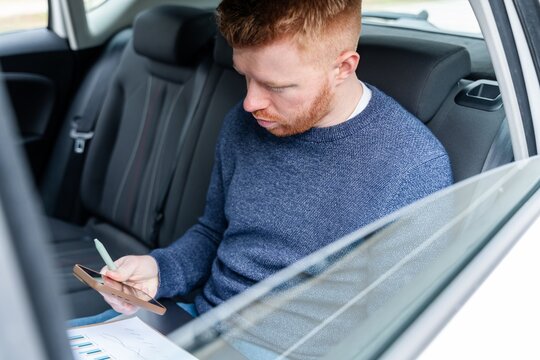 Businessman working on smartphone and reviewing charts in car