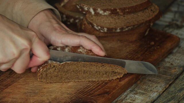 Person cutting a piece of freshly baked rye bread with a knife. Country bread, homemade pastry.
