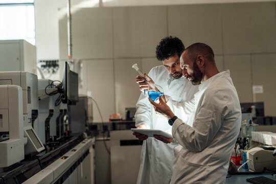 Researchers analyzing blue liquid and tablet in laboratory