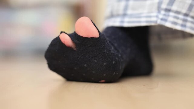 Close-up of a weathered man's foot wearing a torn grey sock on worn wooden floor