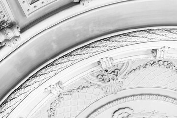 Black and white photograph of an ornate architectural ceiling featuring decorative plaster molding, rosettes and geometric patterns that convey elegance, history and classic interior craftsmanship © evannovostro