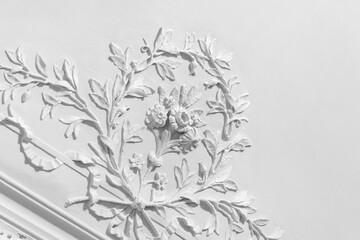Ornate white plaster floral relief adorns a classical ceiling with detailed decorative molding and cornice work, evoking baroque and rococo interior architecture, vintage and elegant craftsmanship © evannovostro