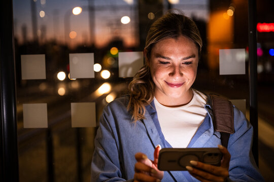 Smiling commuter using smartphone at bus stop at night